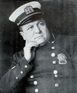 Black and white photograph portrait of Joseph Petrosino. He is wearing a police uniform. He is clean shaven. He's posed with his right hand under his jaw.